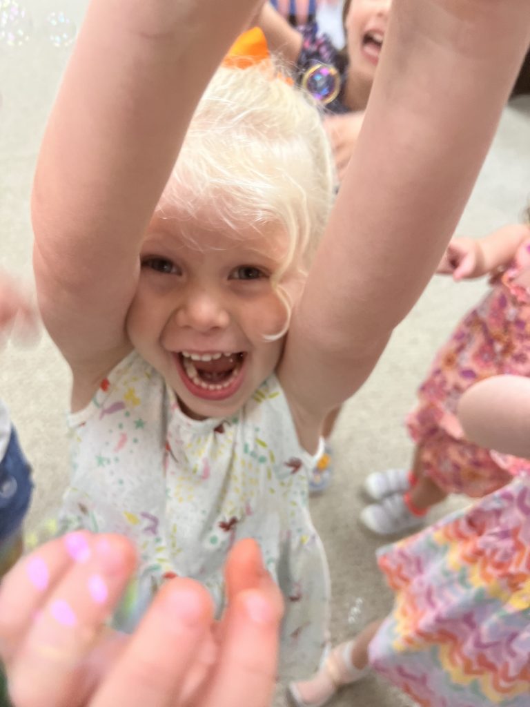 An excited child smiles while raising her arms in the air.